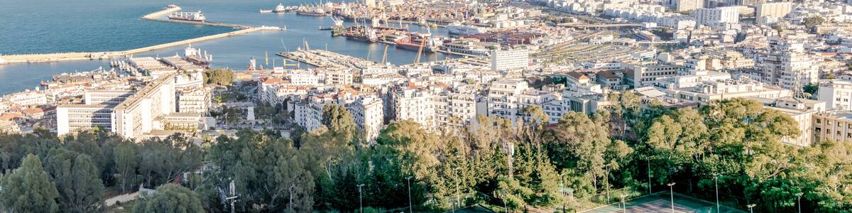Algiers sea bay and pier port, aerial view on the capital city buildings, trees and Mediterranean blue water ships and boats. The Great mosque and the Martyr's Memorial monument.