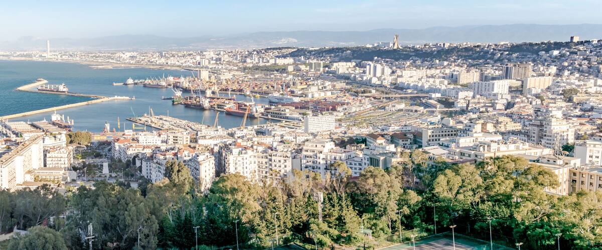 Algiers sea bay and pier port, aerial view on the capital city buildings, trees and Mediterranean blue water ships and boats. The Great mosque and the Martyr's Memorial monument.