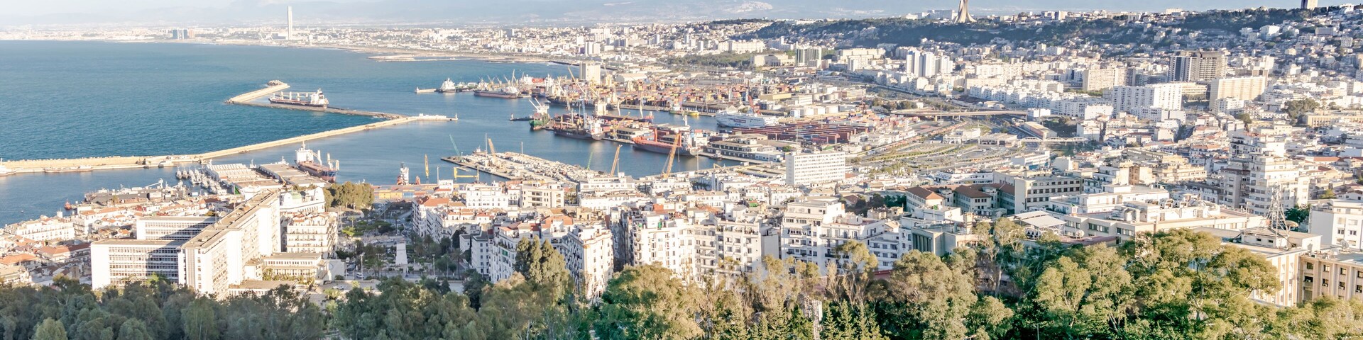 Algiers sea bay and pier port, aerial view on the capital city buildings, trees and Mediterranean blue water ships and boats. The Great mosque and the Martyr's Memorial monument.