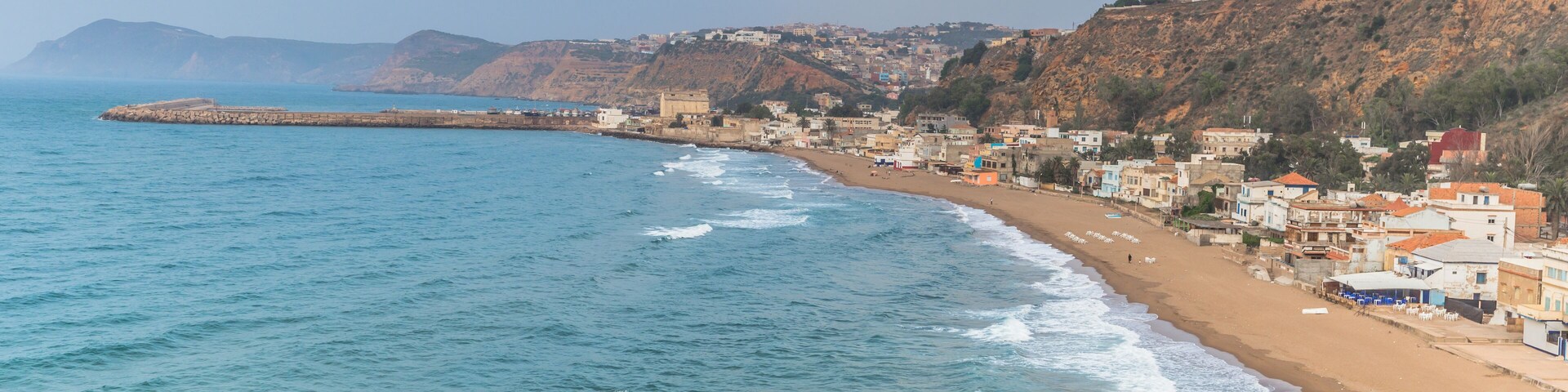 Un pueblo costero con playa, casas y una ladera rocosa.