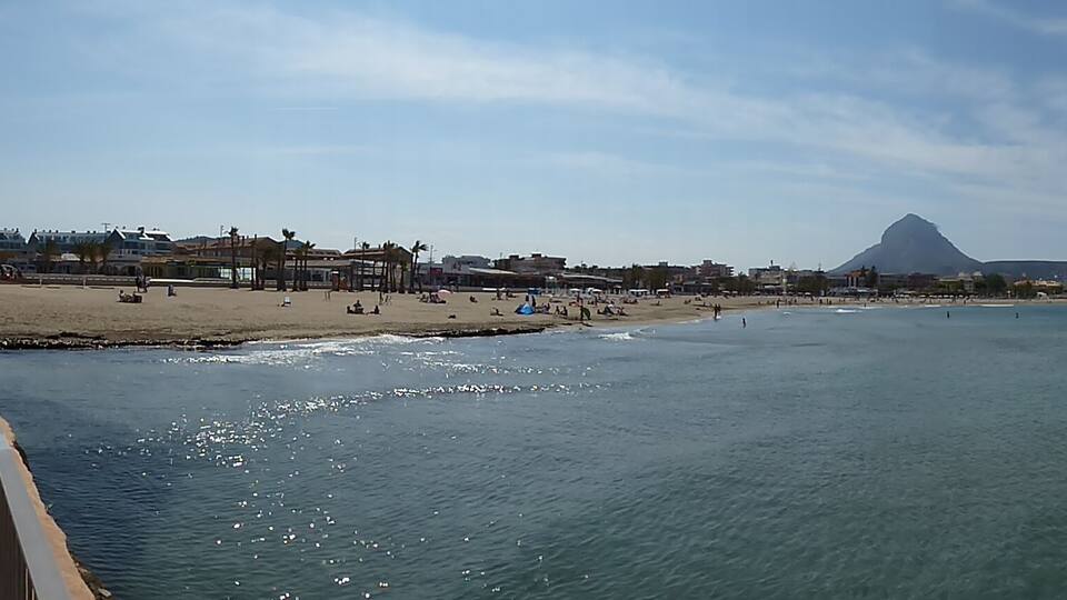 A coastal cityscape with a beach, promenade, and a prominent mountain in the background.