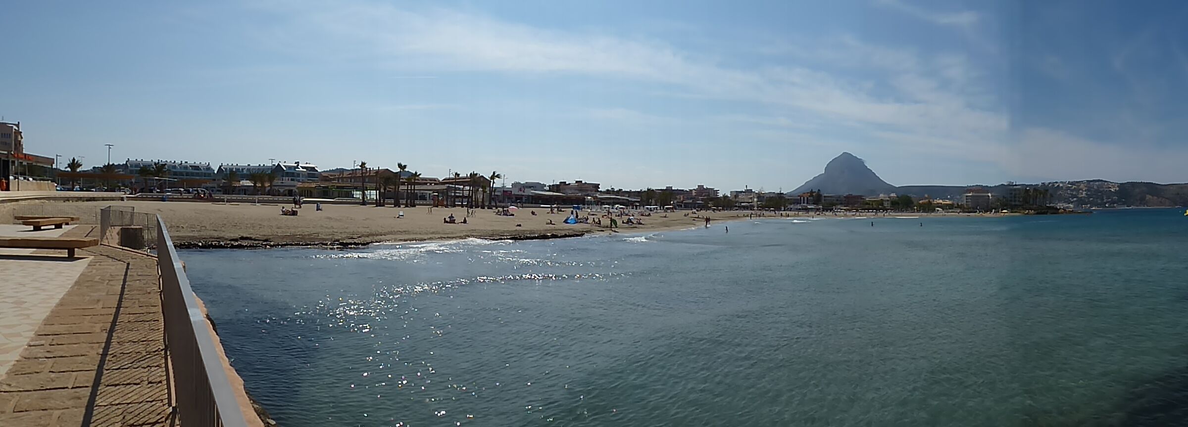 A coastal cityscape with a beach, promenade, and a prominent mountain in the background.