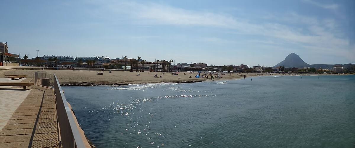 A coastal cityscape with a beach, promenade, and a prominent mountain in the background.