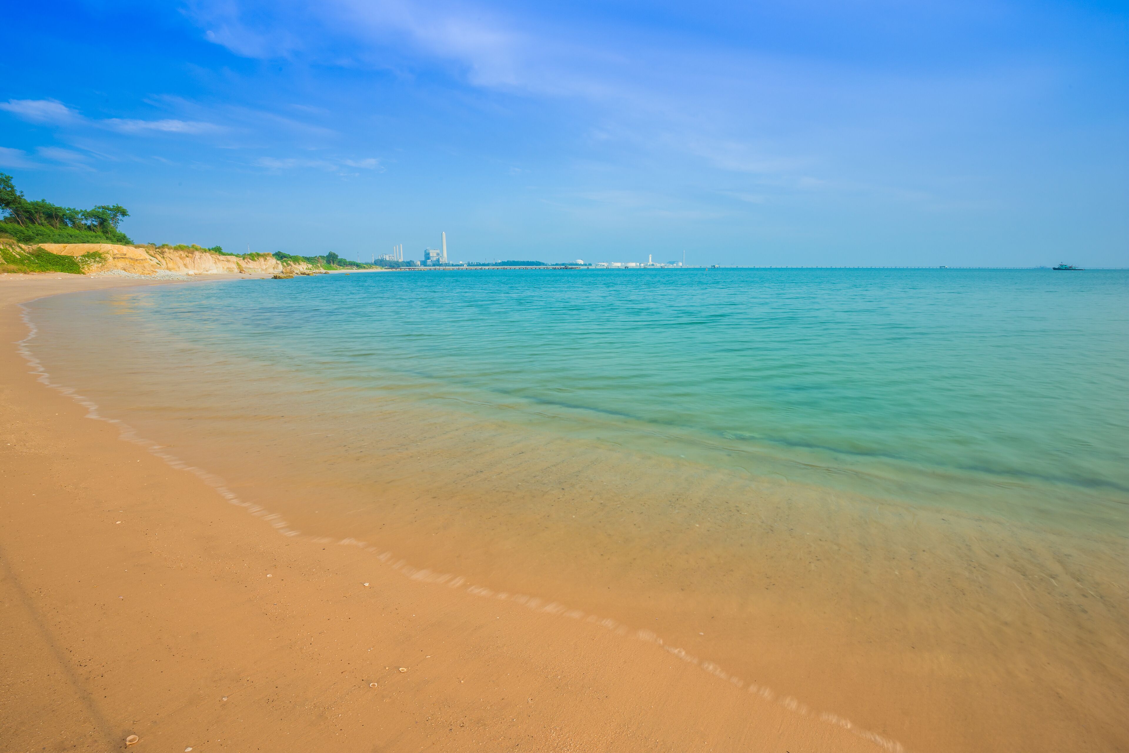 A sandy beach with clear turquoise water and a distant city skyline.