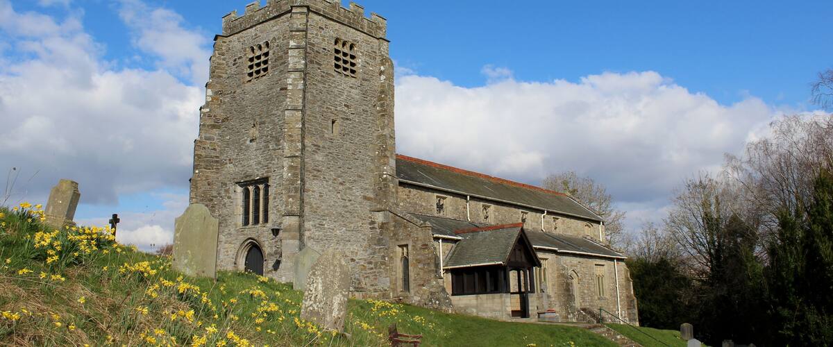 A stone church with a bell tower, surrounded by grass and flowers.