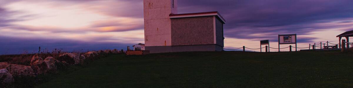 Un phare sur une colline verdoyante, sous un ciel violet.