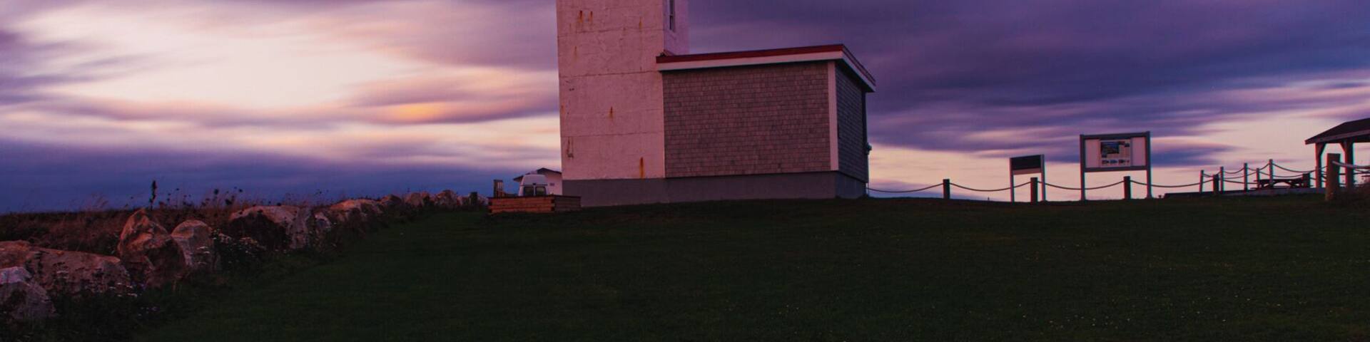 A lighthouse on a grassy hill with a purple sky.