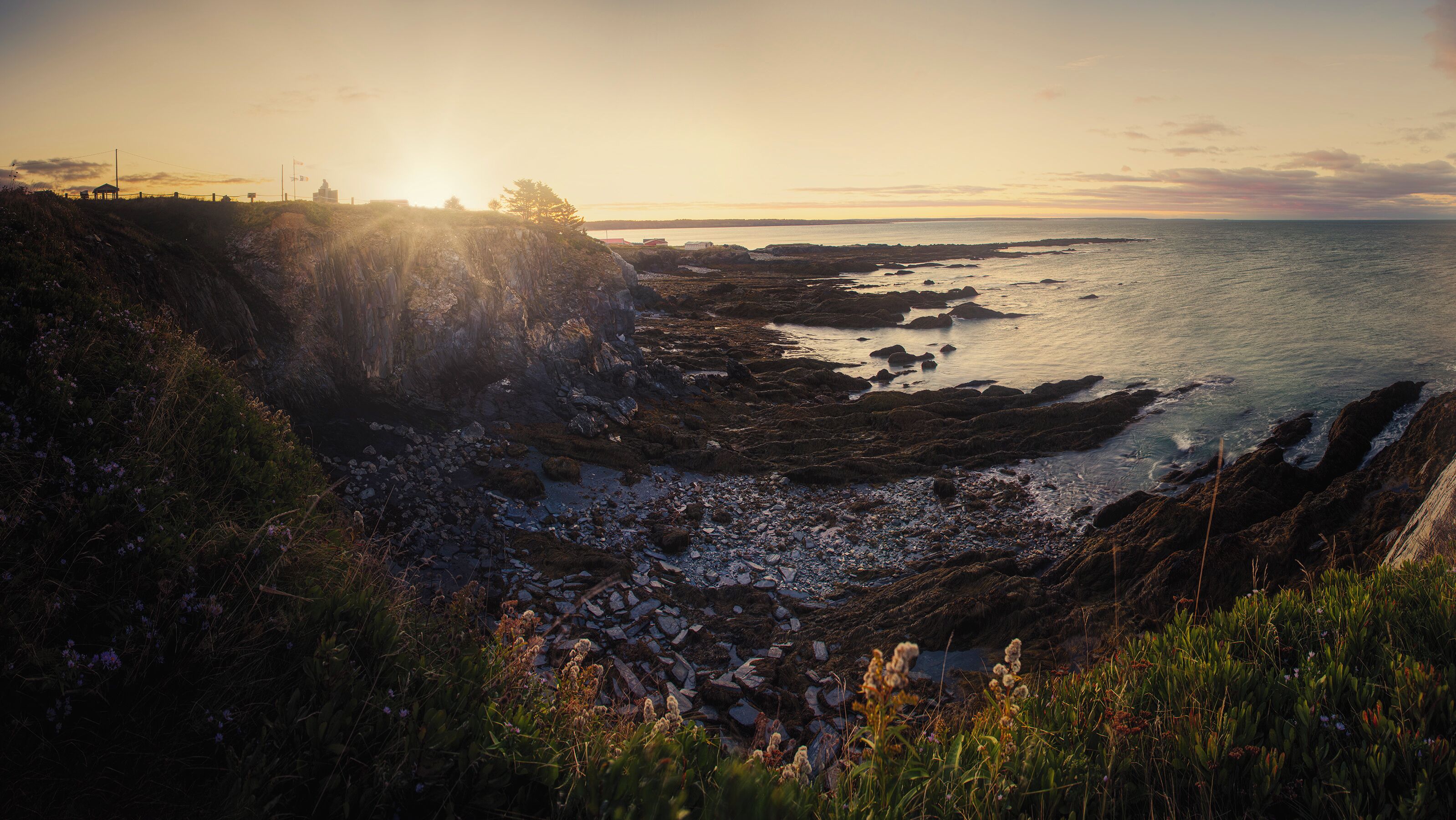 A coastal landscape with rocky shores, a cliff, and the ocean at sunset.
