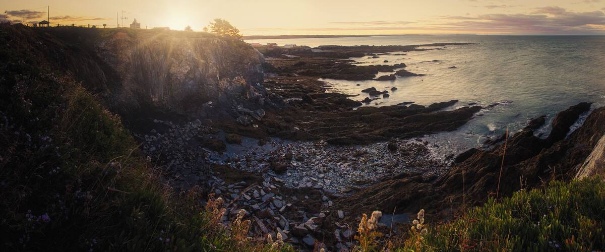 A coastal landscape with rocky shores, a cliff, and the ocean at sunset.