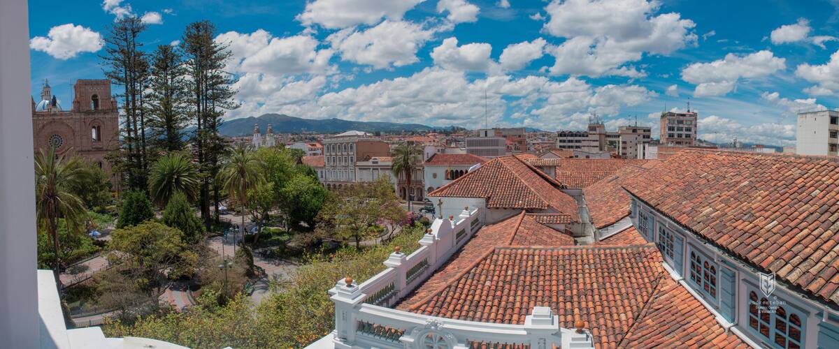 A cityscape with red-tiled roofs, a church with a dome, and a mountainous background.