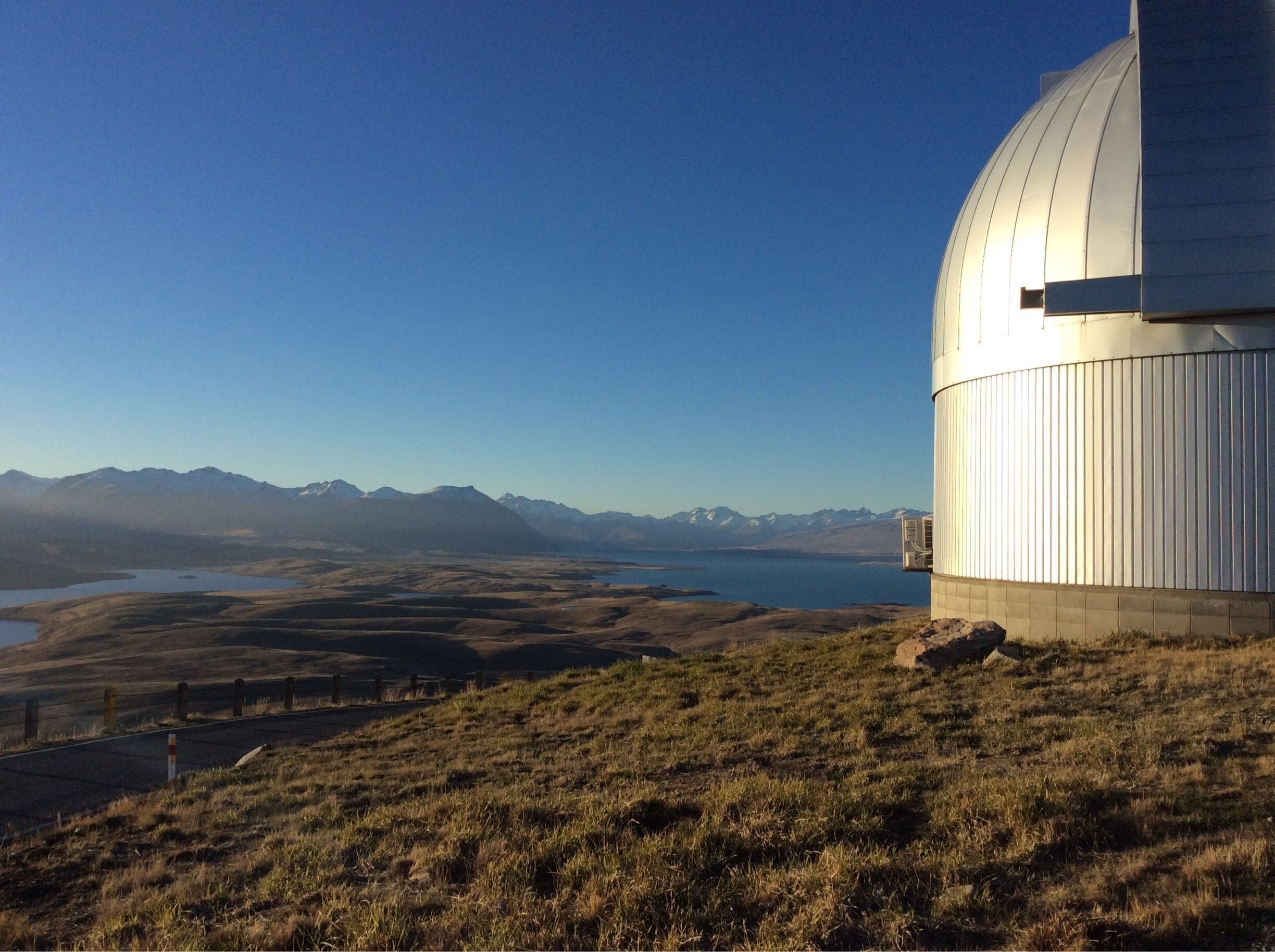 A telescope on a hill overlooking a lake and mountains.