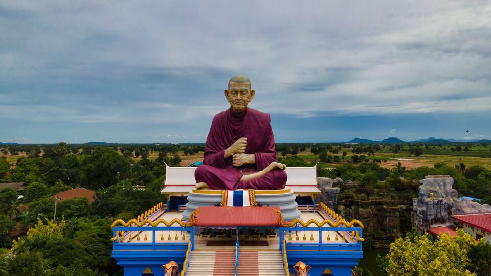 A large statue of a seated figure on a temple roof, surrounded by lush greenery and distant mountains.