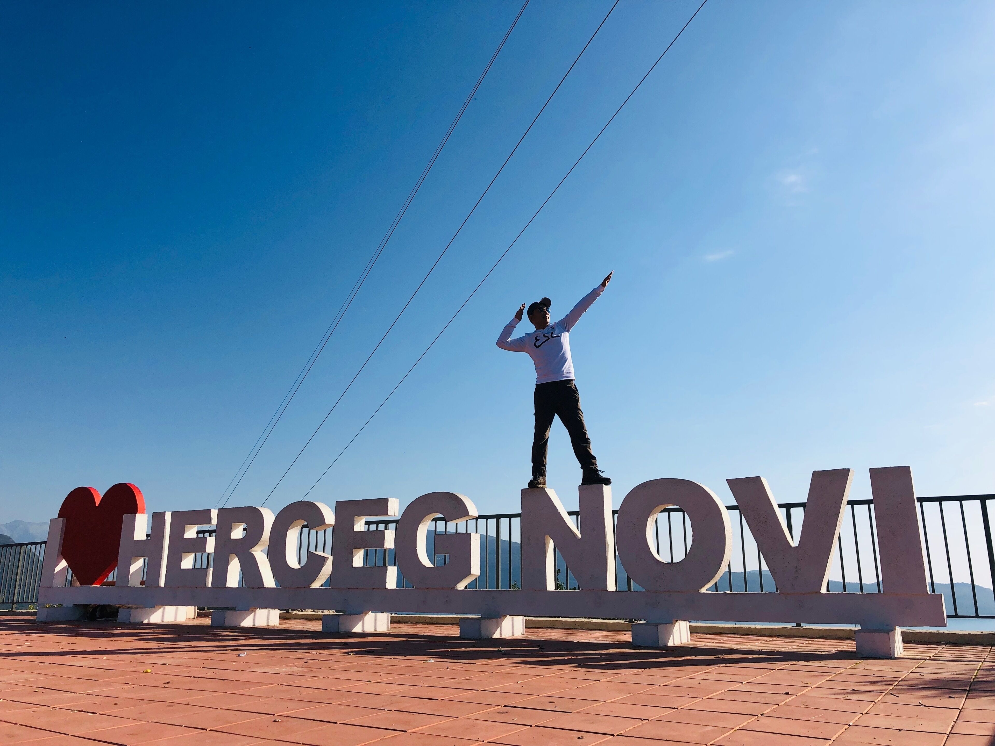 A person standing on a platform with a sign that reads "HERCEG NOVI".