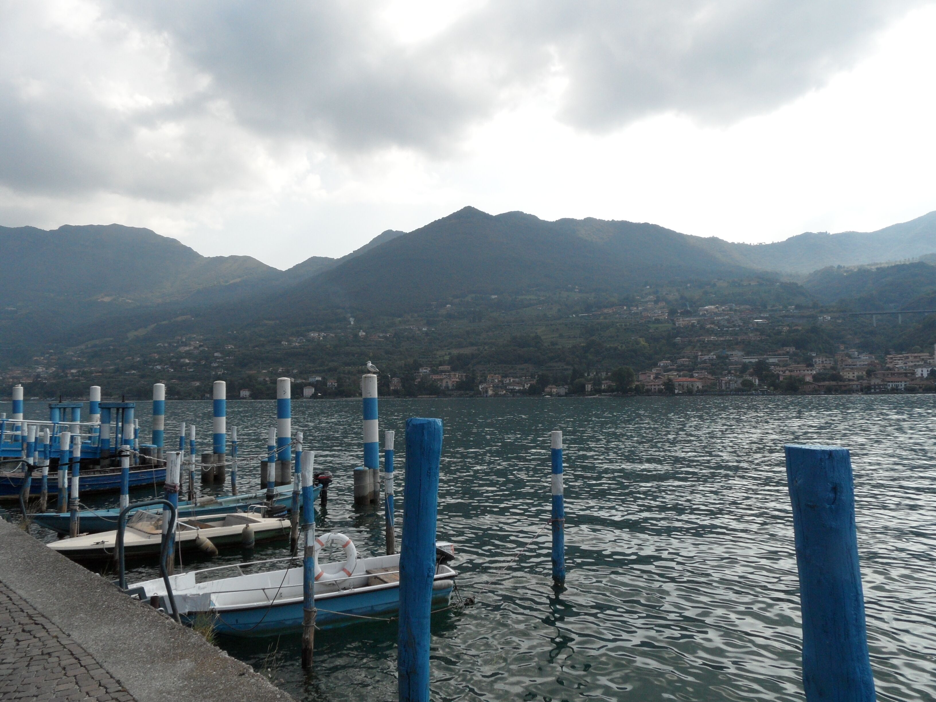 A marina with boats docked, a pier, and mountains in the background.