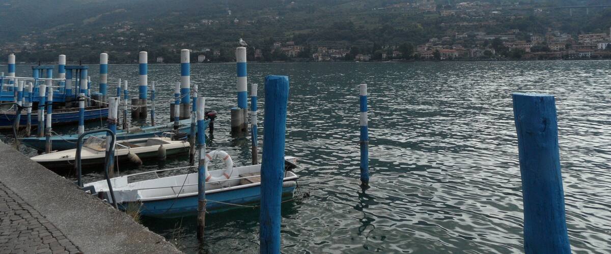 A marina with boats docked, a pier, and mountains in the background.