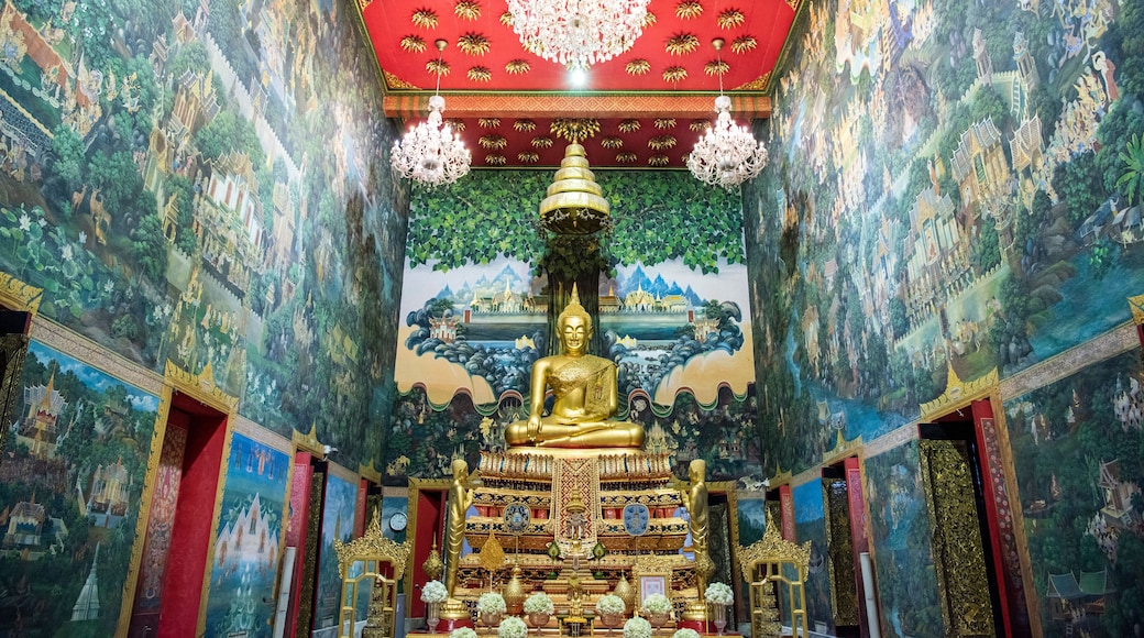 Una estatua dorada de Buda en un templo con murales intrincados y techo rojo.