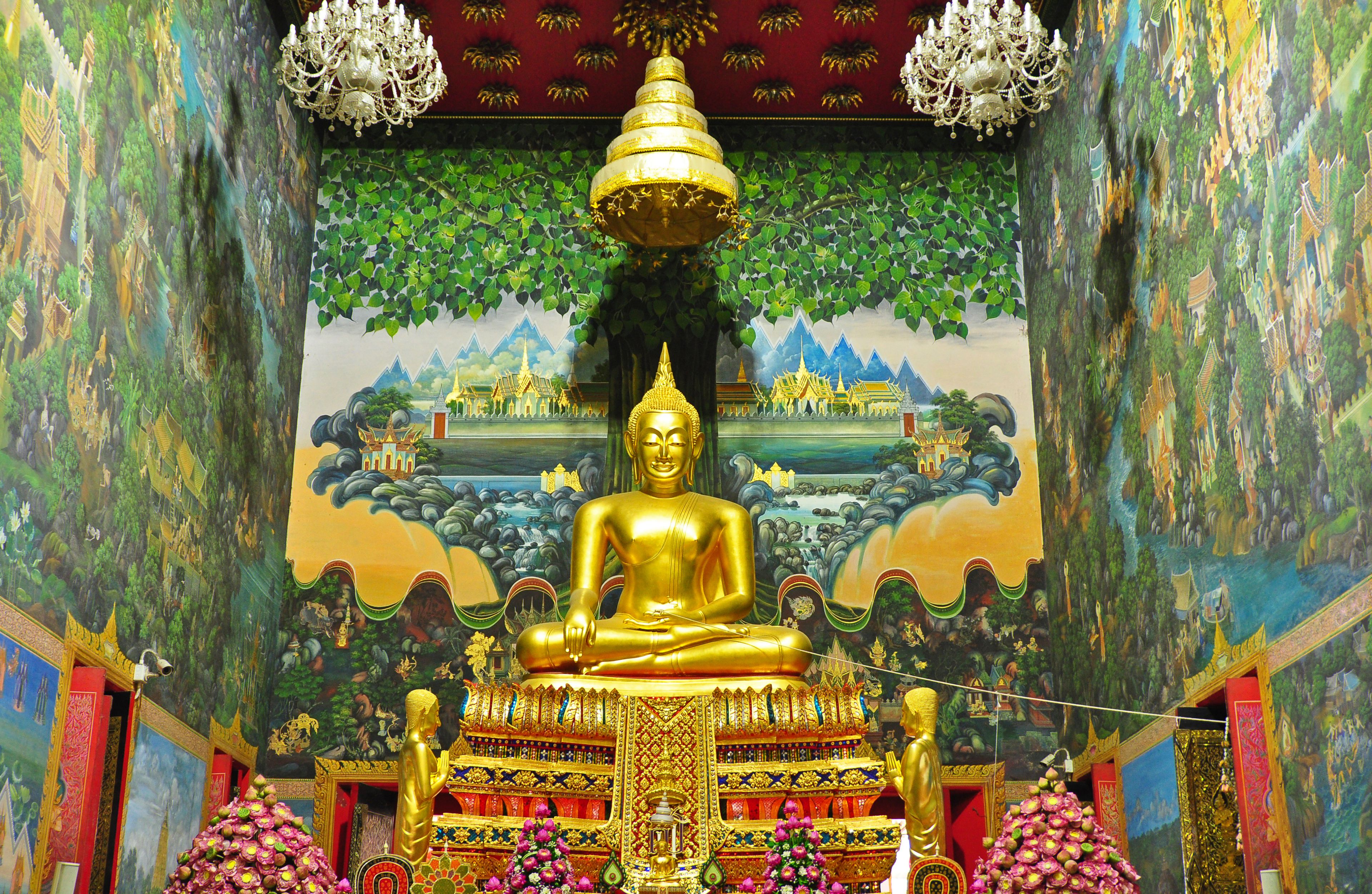 Una estatua dorada de Buda en un templo con murales intrincados y arquitectura tradicional.
