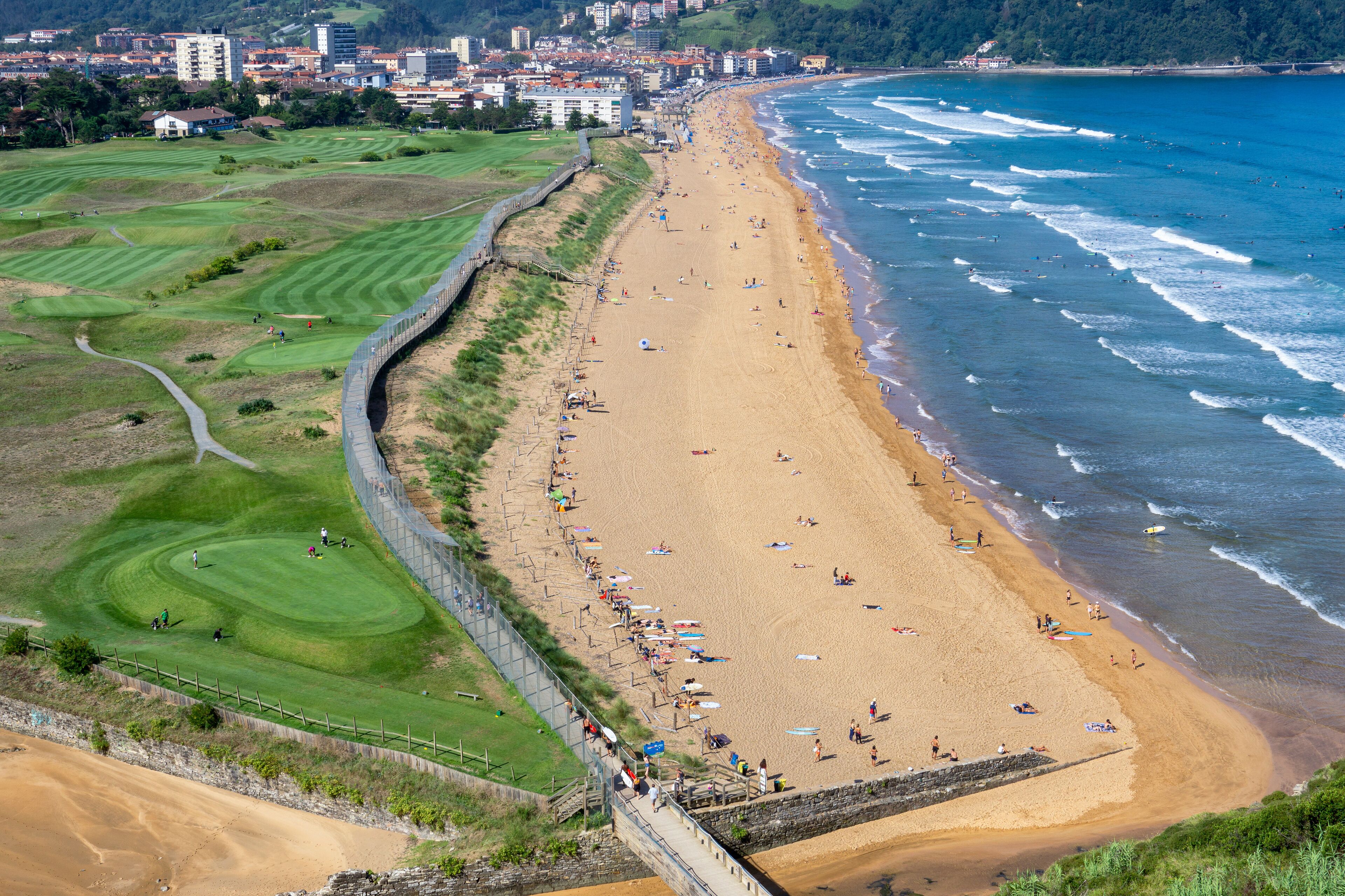 A coastal beach with a golf course and a city in the background.