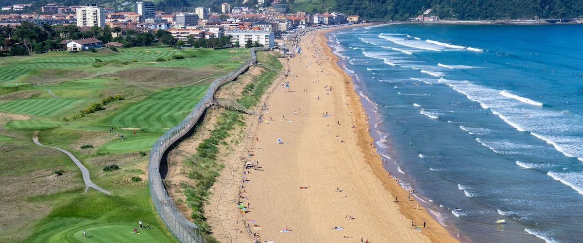 A coastal beach with a golf course and a city in the background.