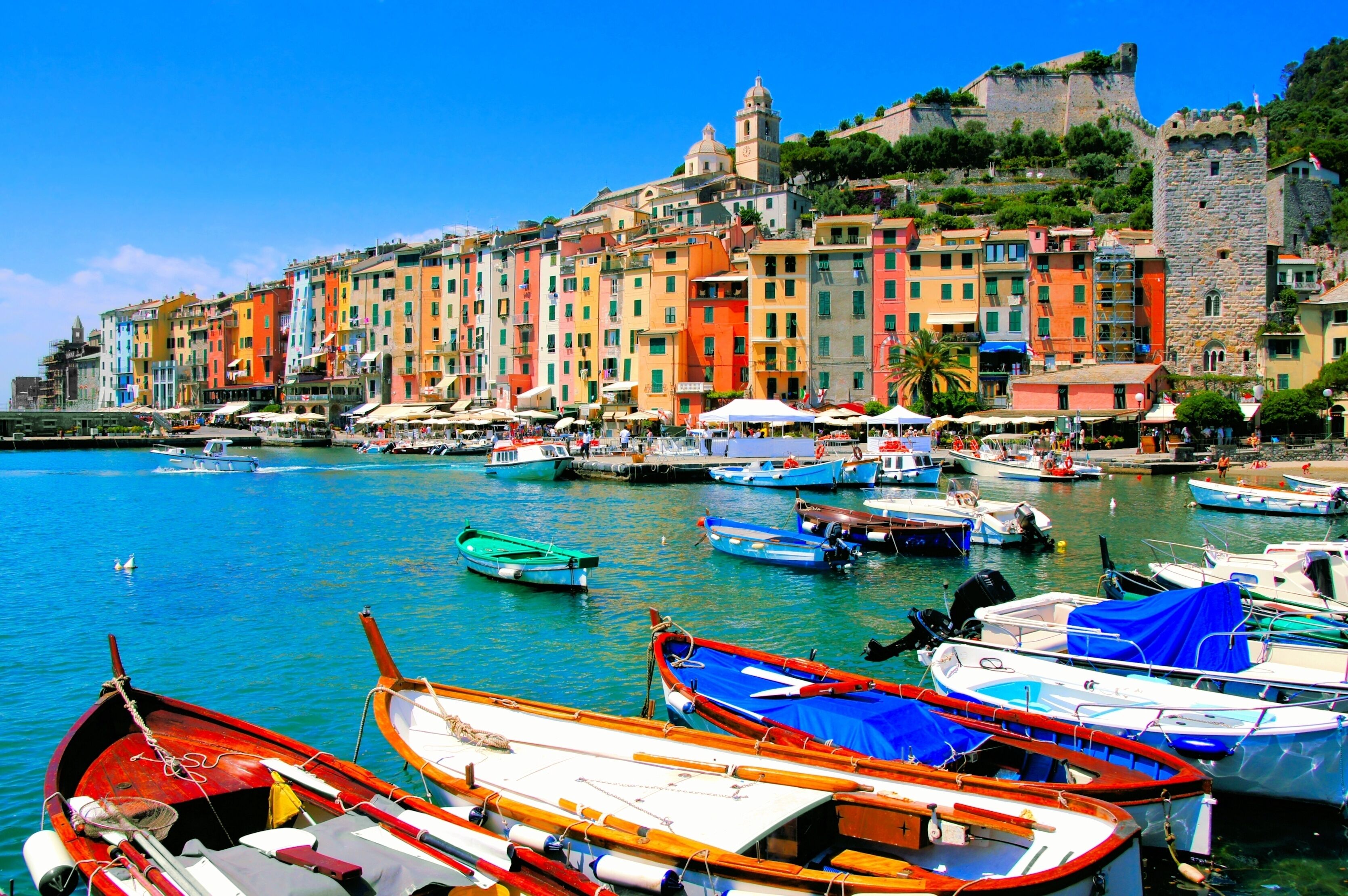 A colorful waterfront with boats docked, a historic building with a tower, and a castle on a hill.