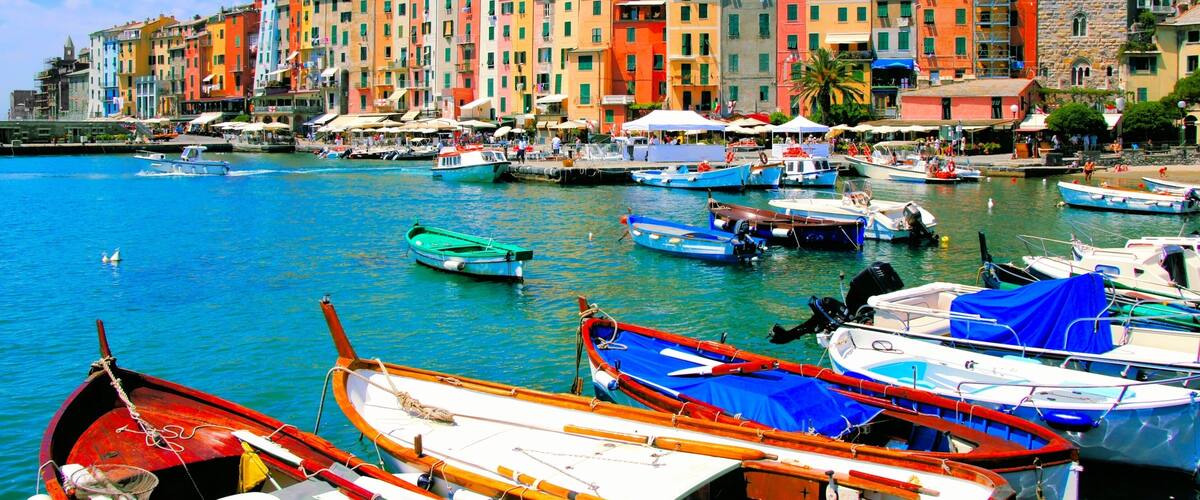 A colorful waterfront with boats docked, a historic building with a tower, and a castle on a hill.