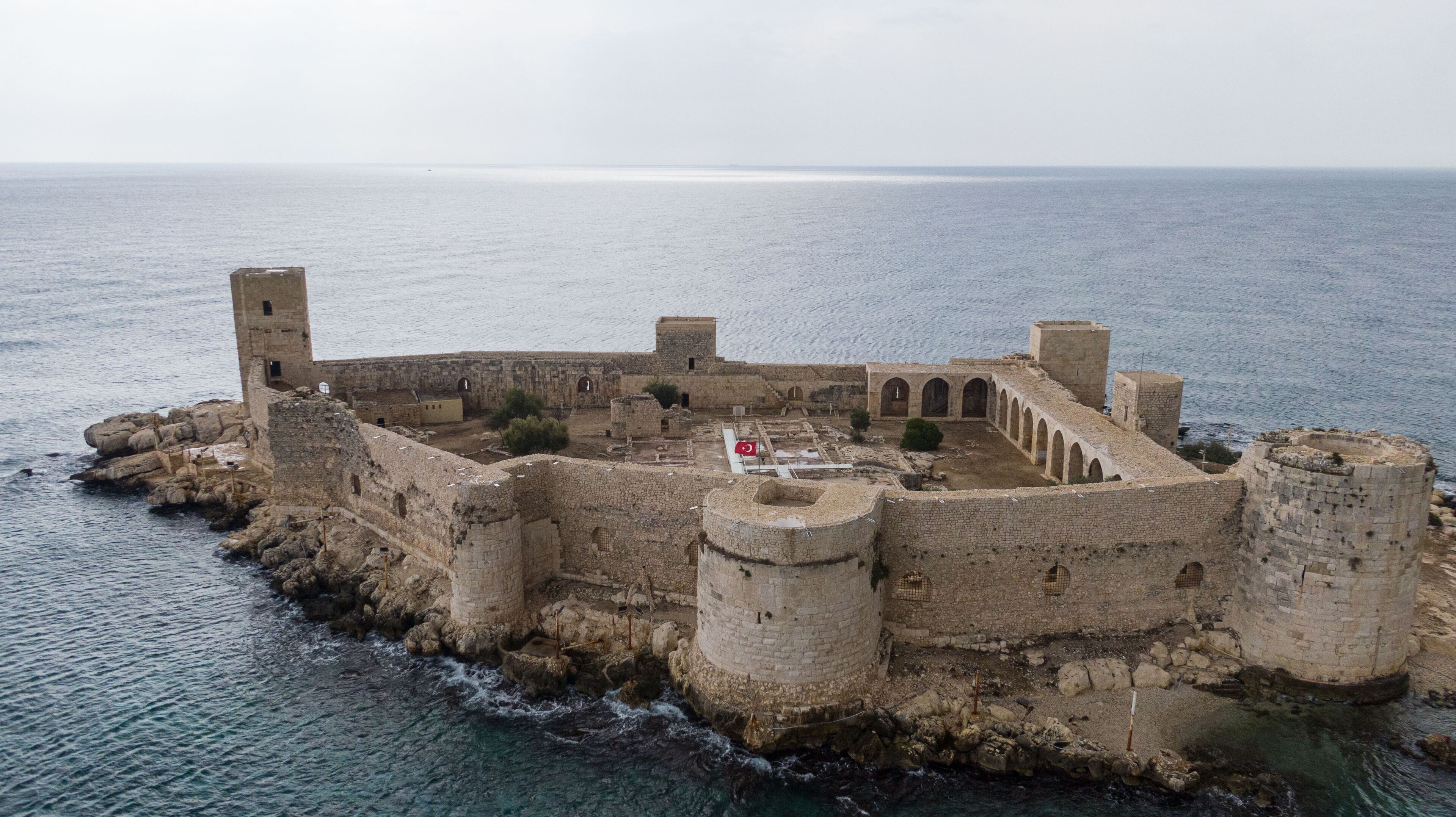 An ancient fortified structure with a flag, surrounded by water.