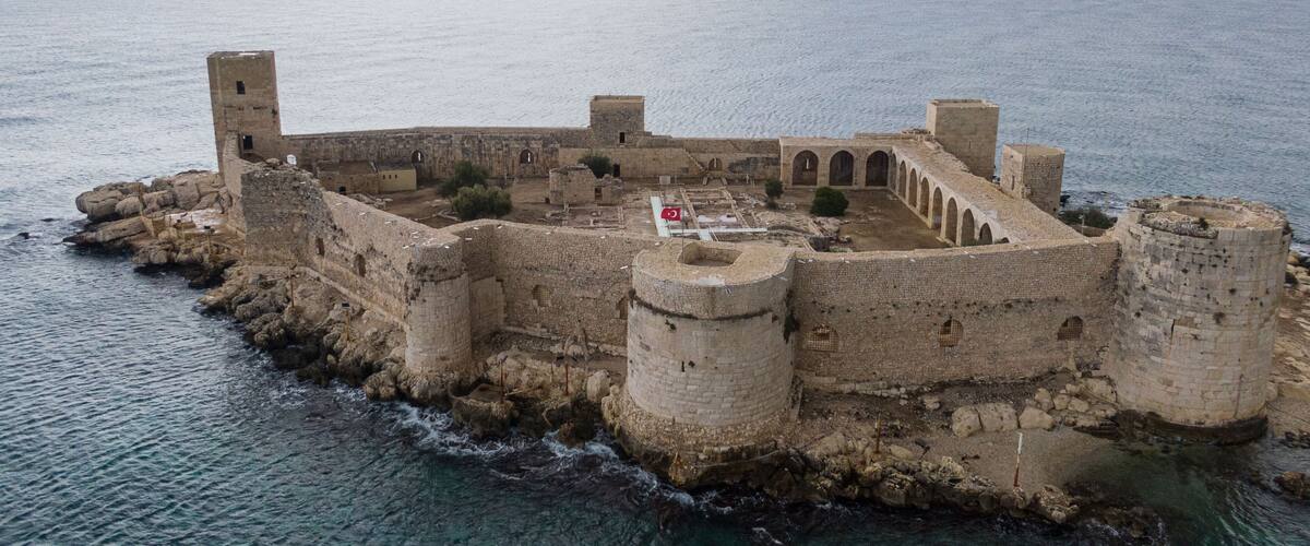 An ancient fortified structure with a flag, surrounded by water.