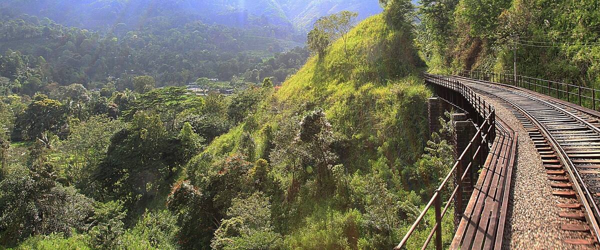 A curved railway track winding through a lush green valley with mountains in the background.