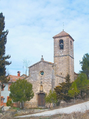 Uma igreja de pedra com uma torre de sino, uma janela circular e uma porta de madeira.