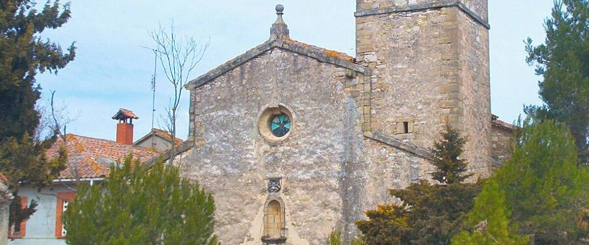 A stone church with a bell tower, a circular window, and a wooden door.