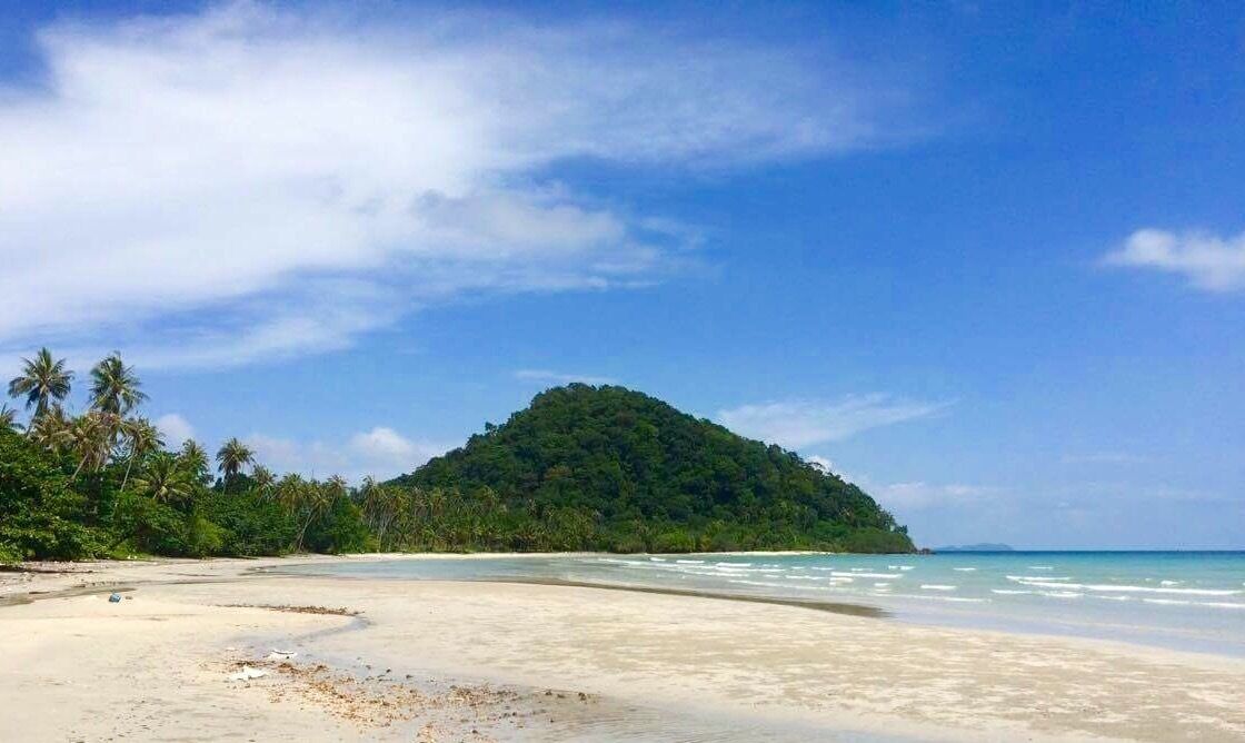 A beach with clear turquoise waters, a sandy shore, and a lush green island in the background.