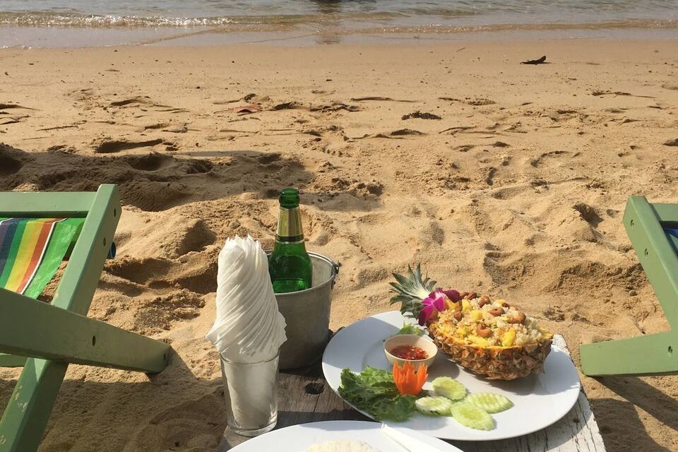 Una playa con una mesa dispuesta con comida, una botella y una silla.
