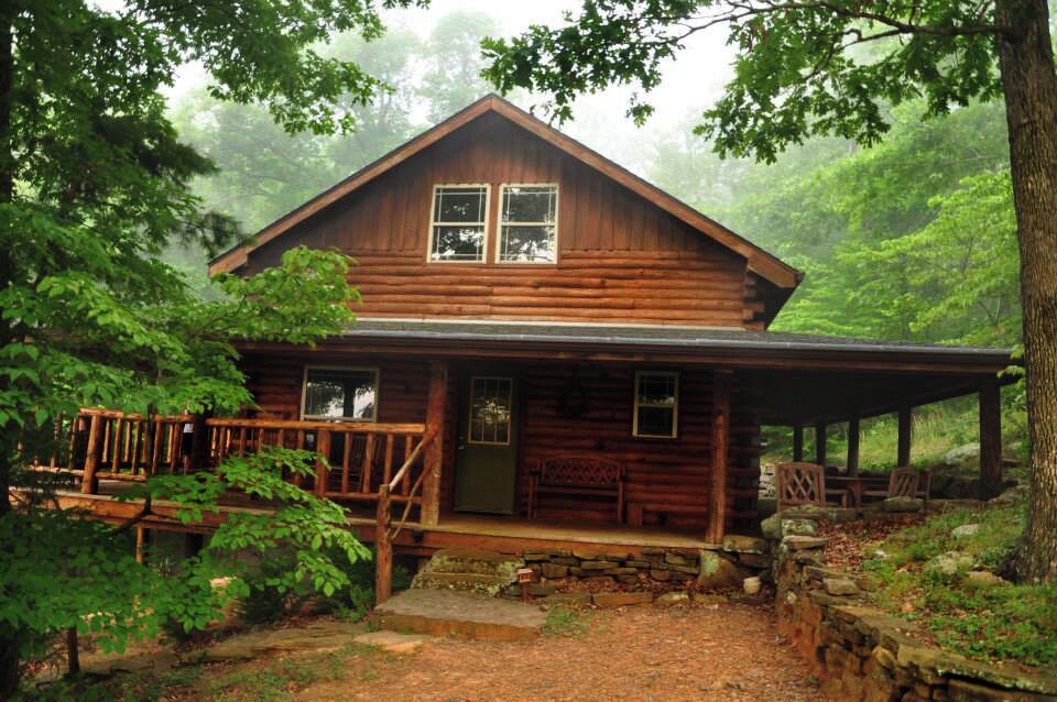 A rustic log cabin surrounded by lush greenery and a stone staircase leading up to the porch.