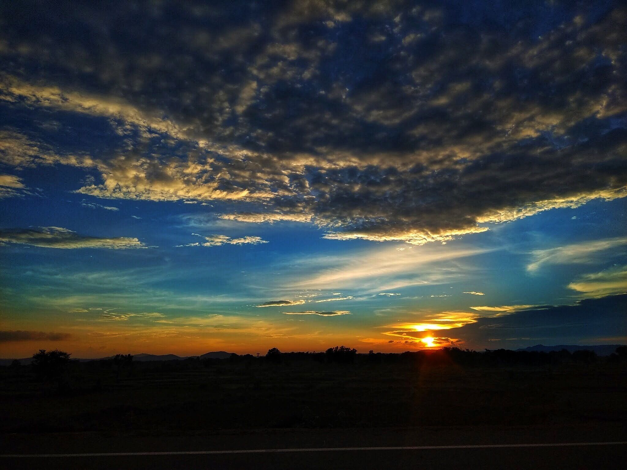A sunset over a flat landscape with a road in the foreground.