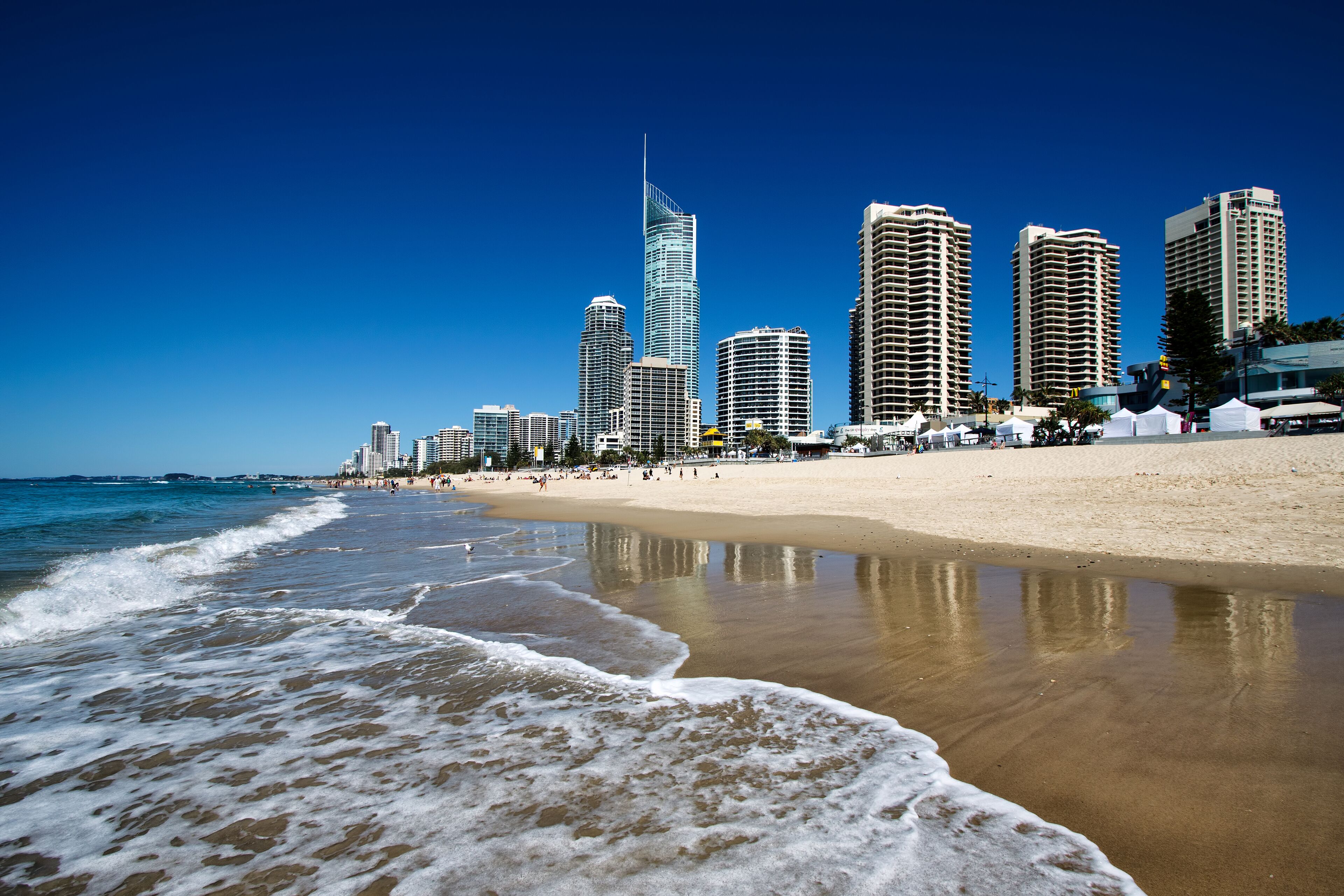 A beach with waves, a sandy shore, and a city skyline with tall buildings.
