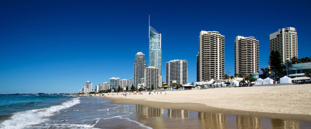 A beach with waves, a sandy shore, and a city skyline with tall buildings.