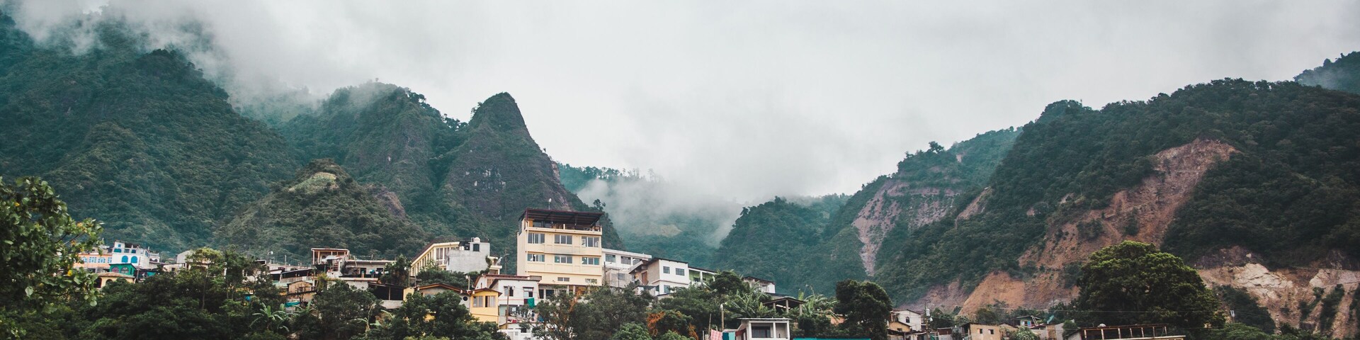Un pueblo montañoso con edificios integrados en exuberante vegetación y nubes.