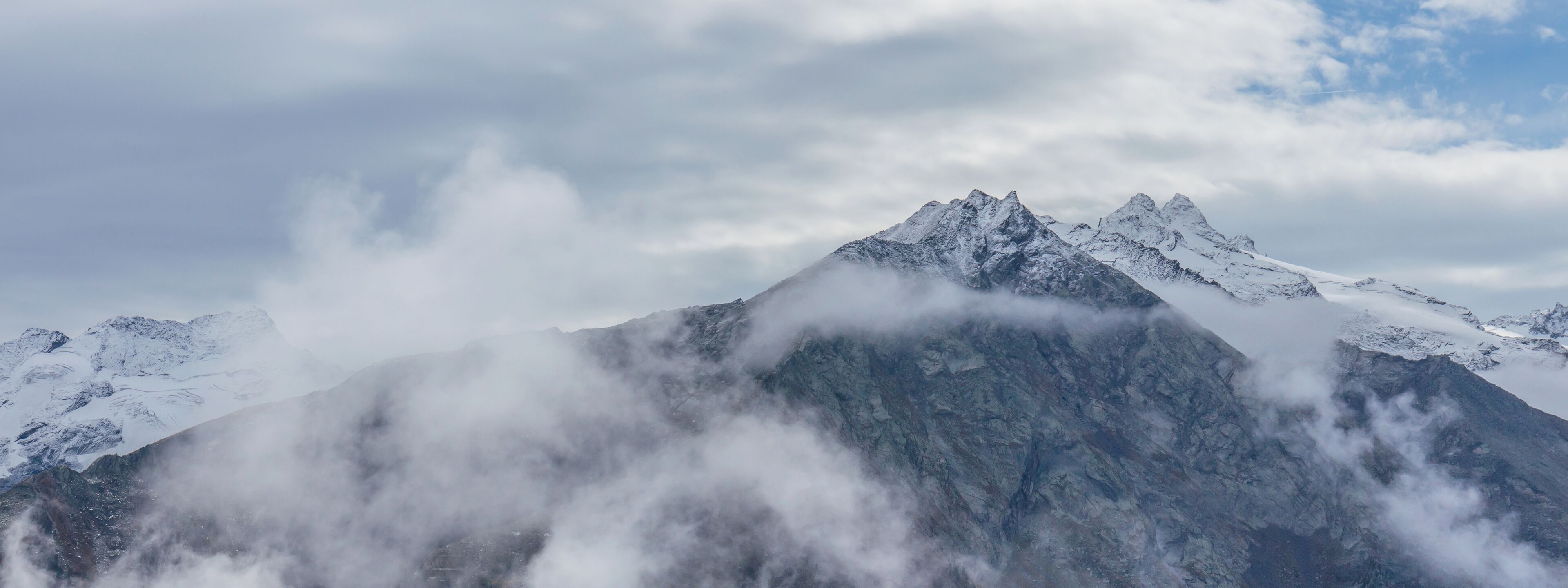 A snow-covered mountain peak with clouds at its base.