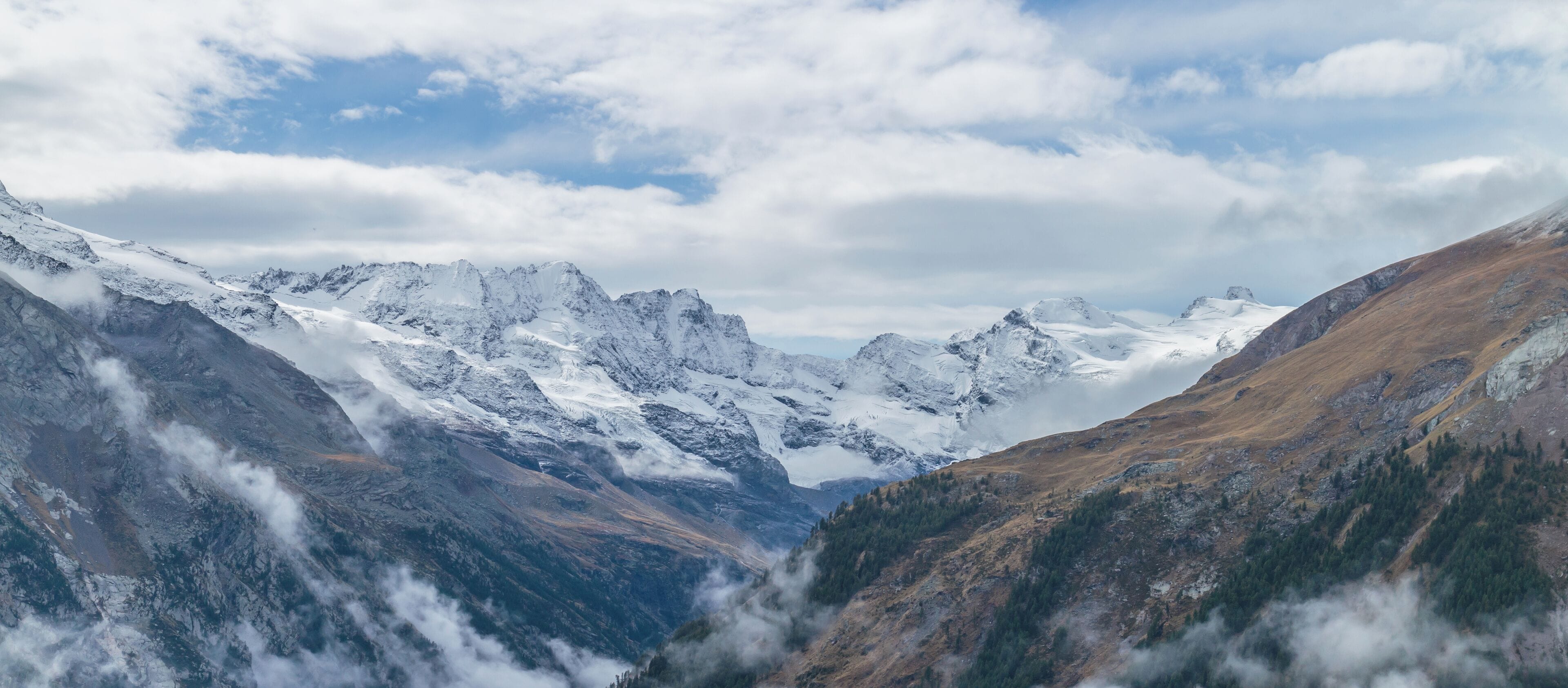 Snow-covered mountains, a valley, and a partly cloudy sky.