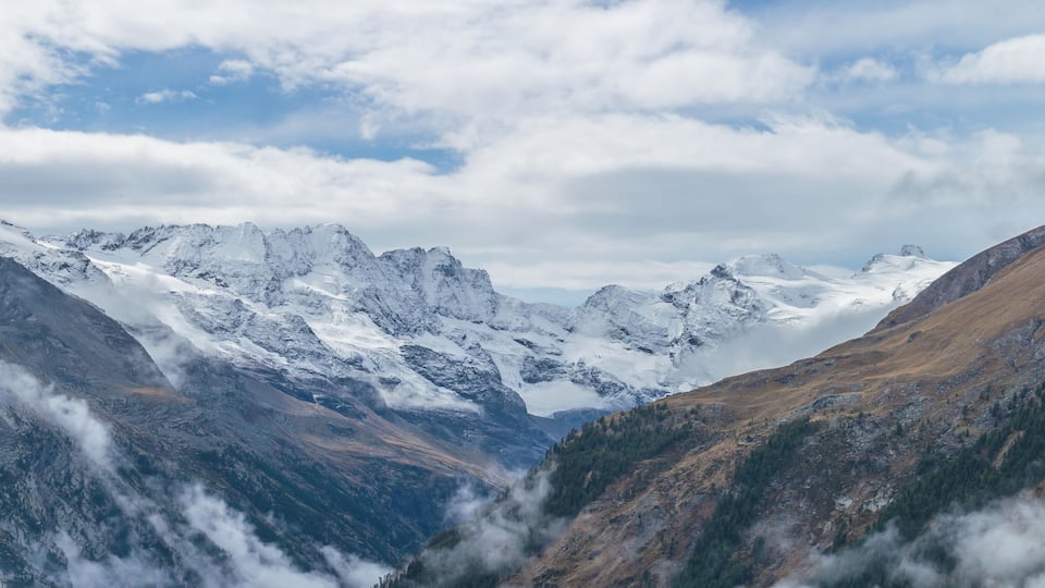 Snow-covered mountains, a valley, and a partly cloudy sky.