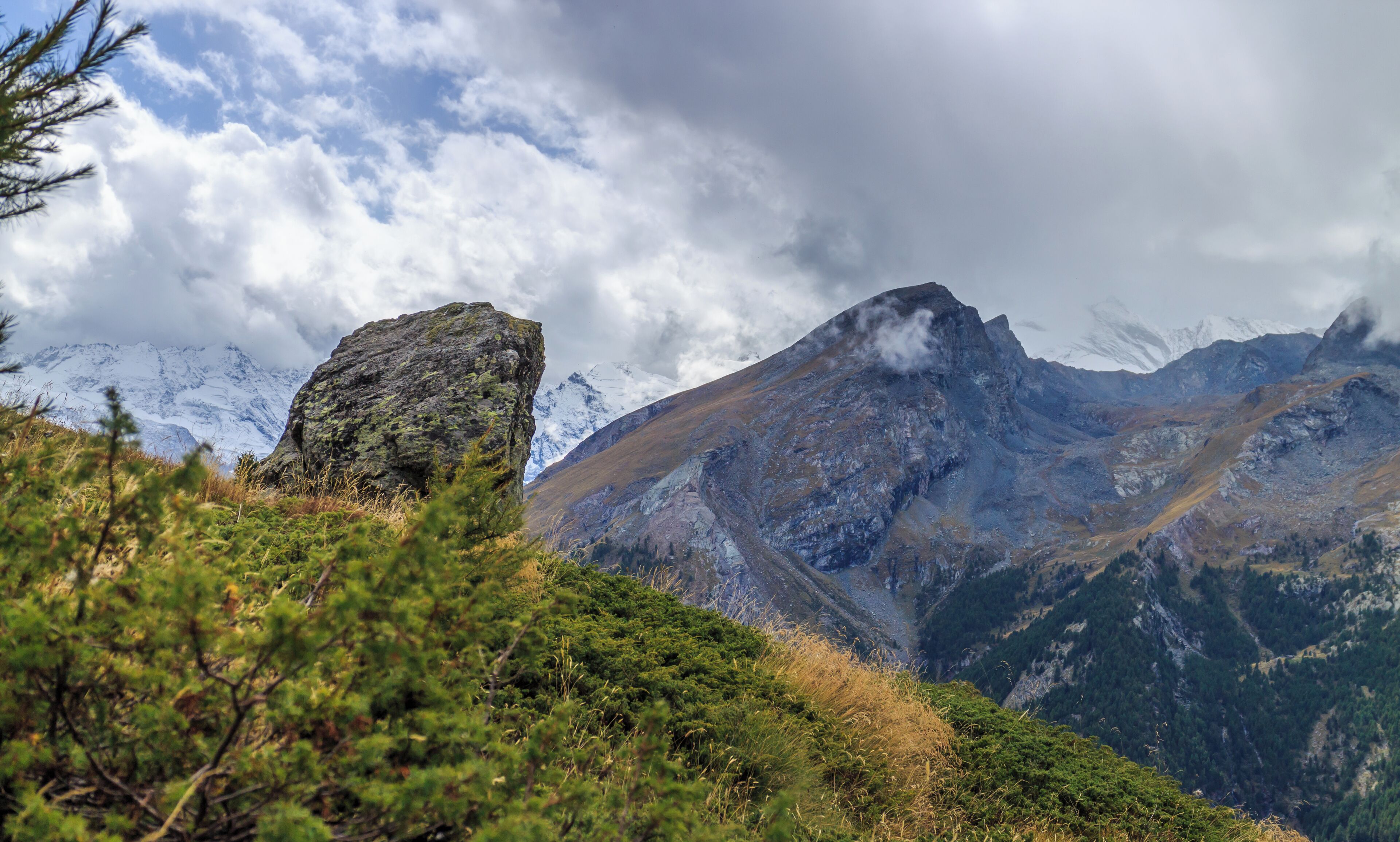 A mountain landscape with a prominent rock formation and snow-capped peaks in the background.