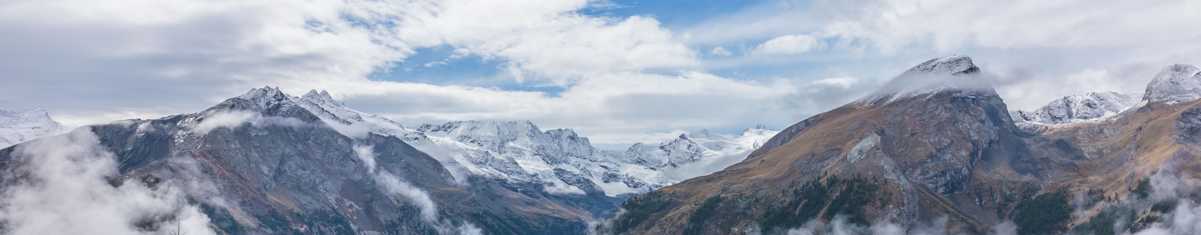 Snow-capped mountains, a valley, and a partly cloudy sky.