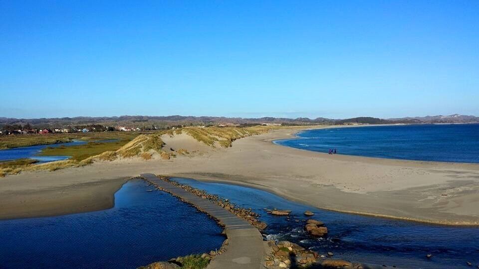 A coastal landscape with a sandy beach, a rocky shoreline, and a clear blue sky.