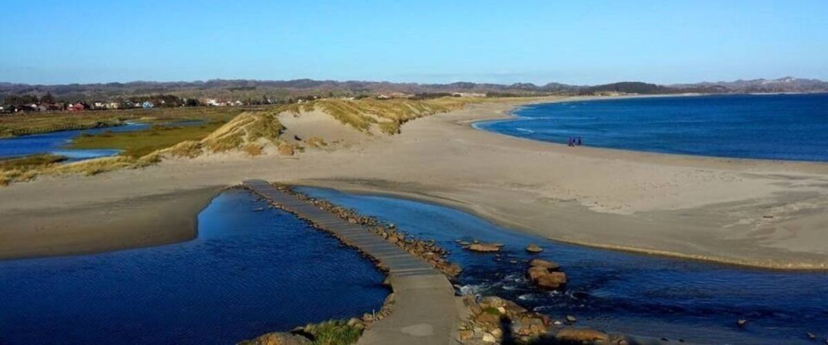 A coastal landscape with a sandy beach, a rocky shoreline, and a clear blue sky.