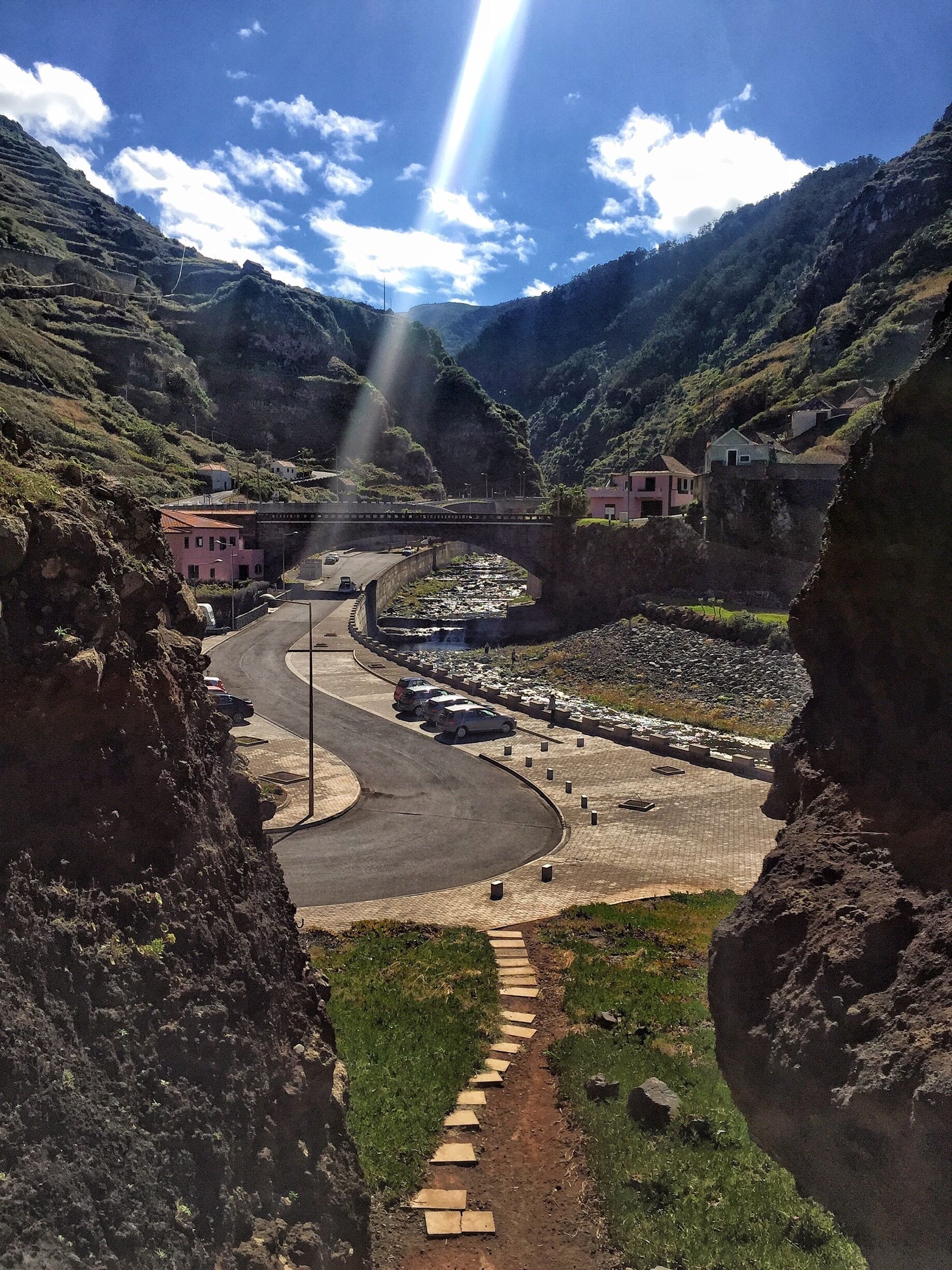 A winding road in a mountainous area with a bridge, houses, and a river.