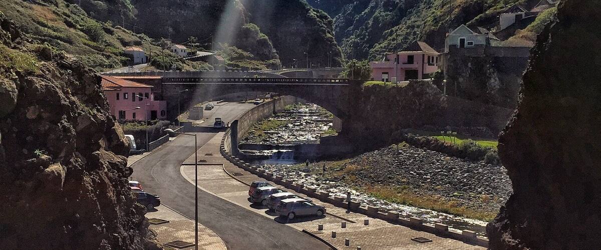 A winding road in a mountainous area with a bridge, houses, and a river.