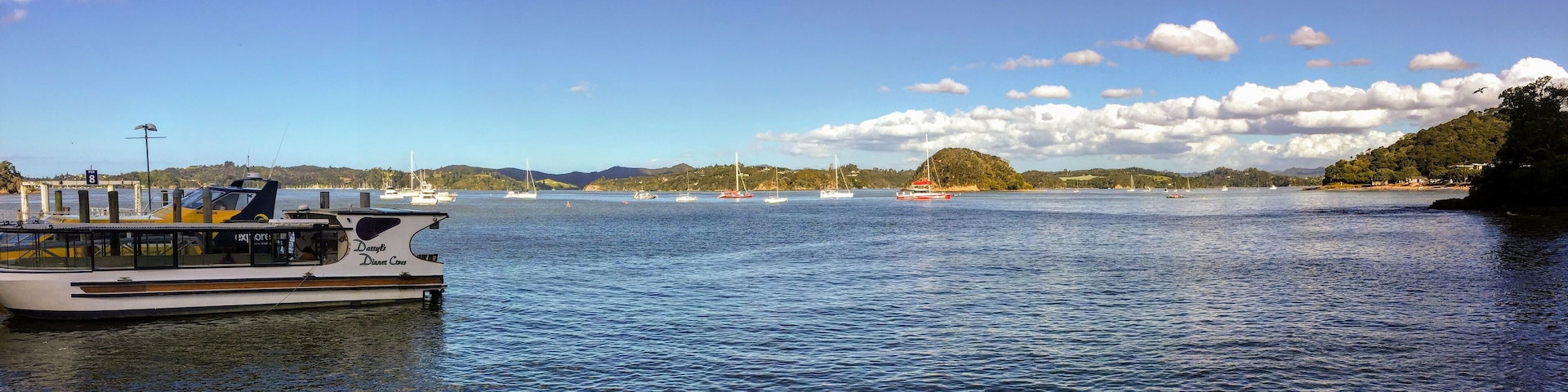 The view of Kororareka Bay in Russell, New Zealand. Many boats are anchored in the bay. The local ferry that takes tourists and locals back and forth to Russell is in view.