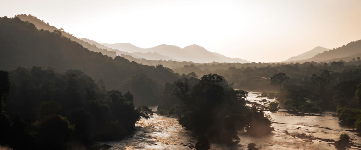 A river flowing through a valley with dense forest and hills in the background.