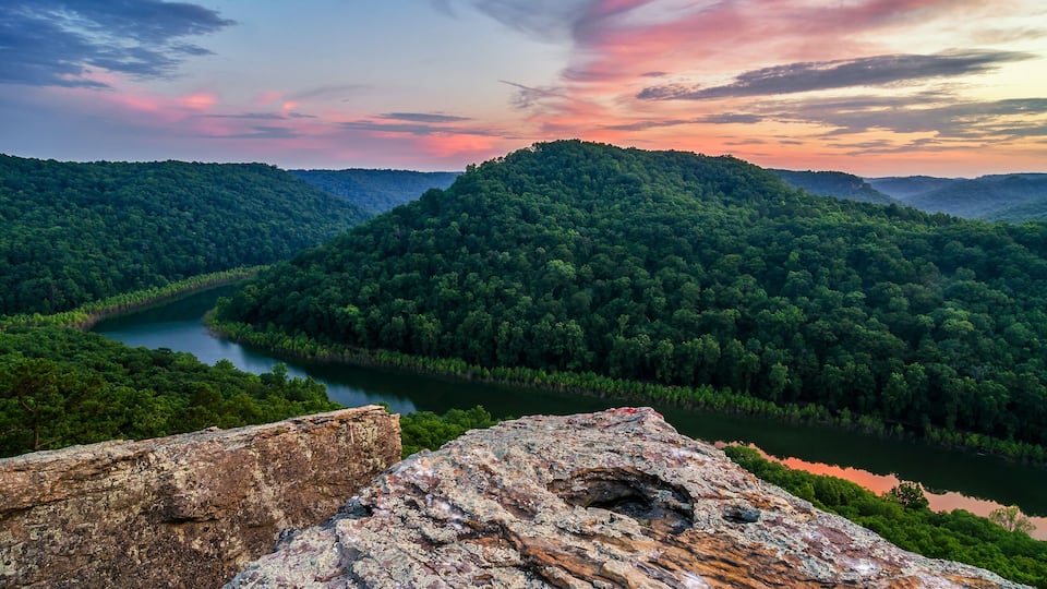A river winding through a forested valley with a rocky foreground.