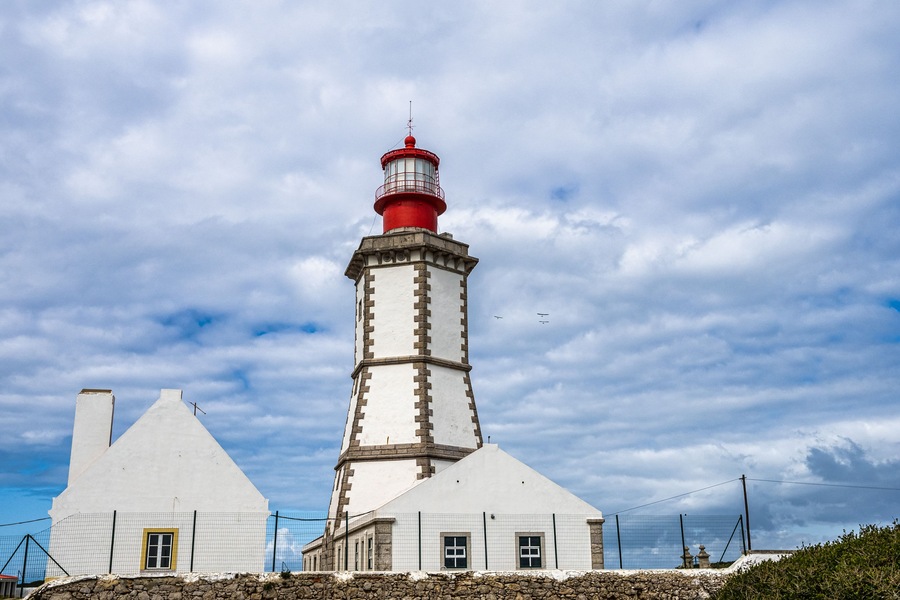 A lighthouse with a red top, white walls, and a stone base.